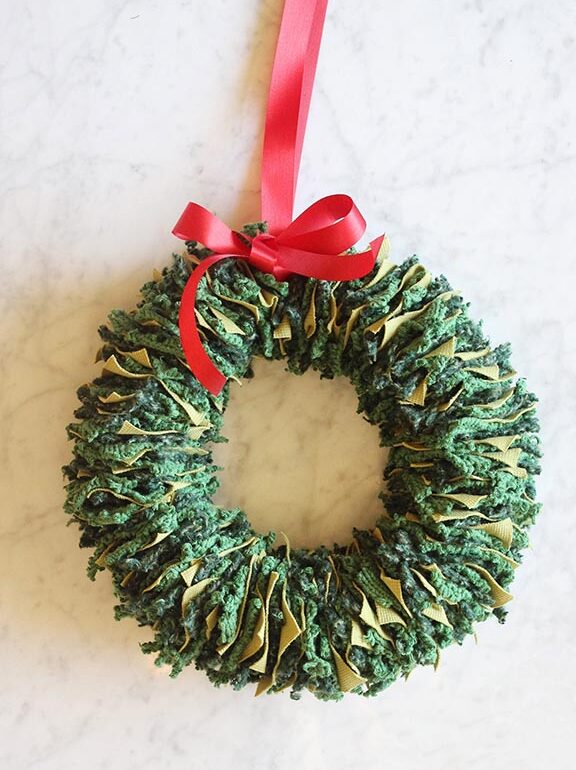 A green wreath with a red ribbon hanging on a marble table.