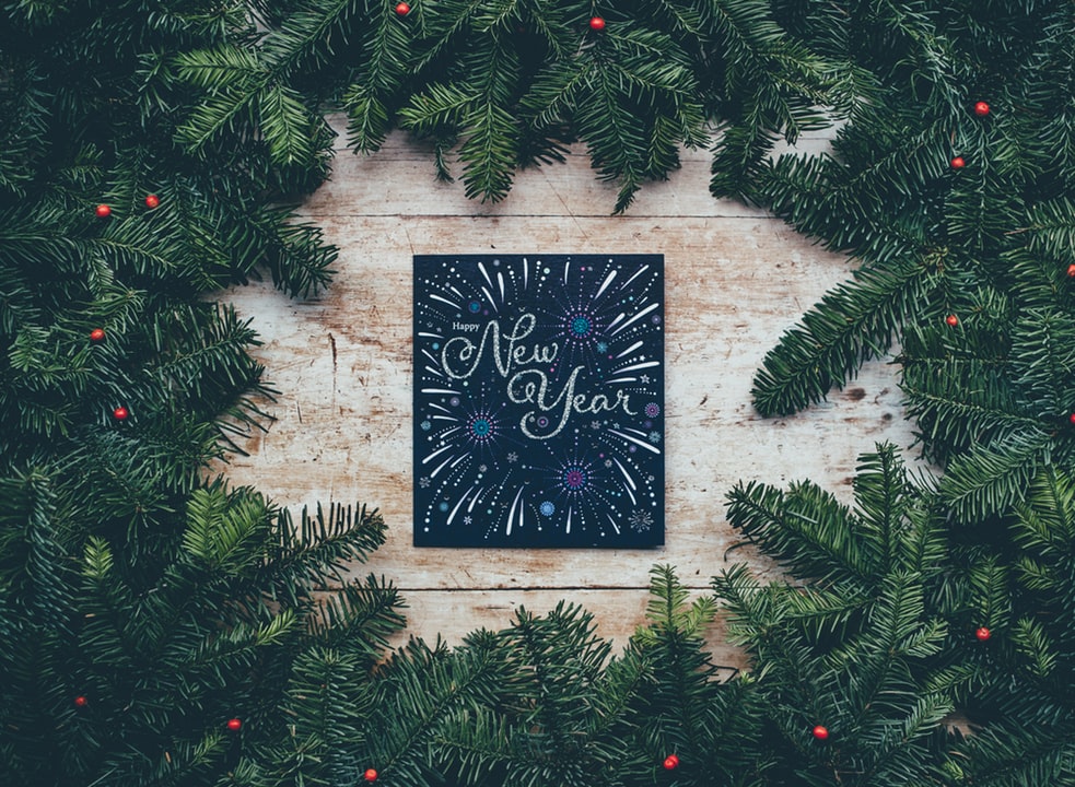 A christmas card with the words new year surrounded by greenery.