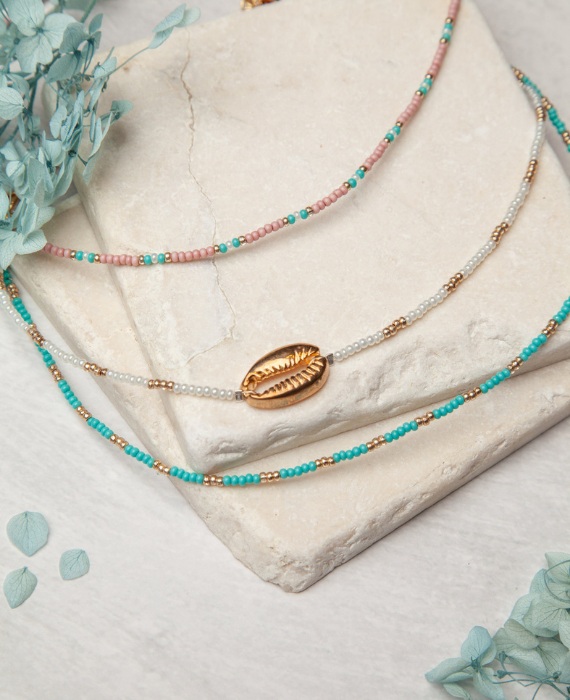 A necklace with a shell and beads on top of a stone.