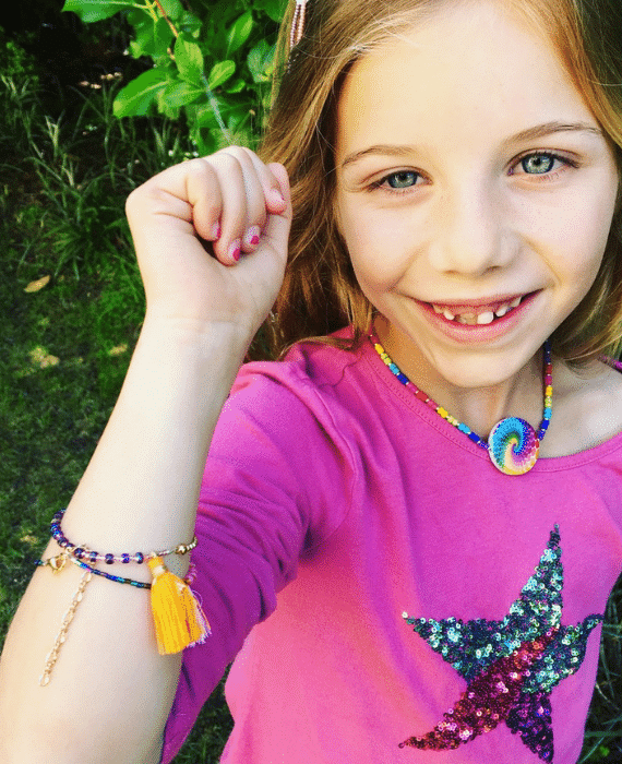 A little girl wearing a pink shirt and tassel bracelet.