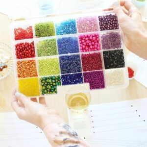 A person holding a colorful beading kit on a table.