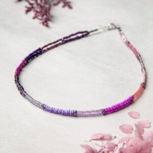 A purple and pink beaded necklace on a white surface.