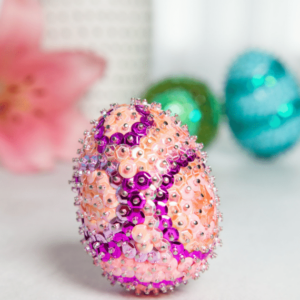 Sequin easter eggs on a table next to a flower.